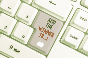 Handwriting text And The Winner Is. Conceptual photo announcing who got first place at competition or exam White pc keyboard with empty note paper above white background key copy space