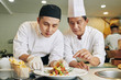 © DragonImages - Asian mature chef holding master class for his student he teaching him to decorate the dish in the kitchen