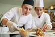 © DragonImages - Young Asian cook decorating prepared salad together with chef in the kitchen of the restaurant