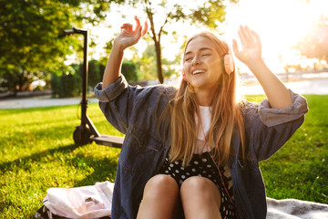 Wall Mural - Girl outside in nature green park on grass listening music with earphones.