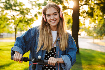 Wall Mural - Positive optimistic young teenage girl outside walking with scooter.