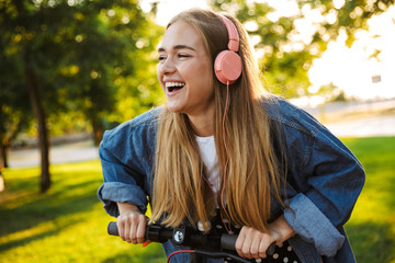 Wall Mural - Positive optimistic young teenage girl outside walking with scooter.