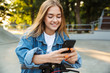 © Drobot Dean - Smiling cheerful teenage girl in park walking on scooter using mobile phone.