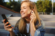 Teenage girl in park sit on steps using mobile phone listening music with earphones.
