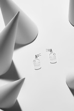 Close-up Shot Of A Pair Of Sweet Stud Earrings With Dangling Flat Glassy Plates In The Form Of A Bottle With Lettering "water".  