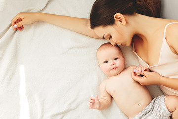 Wall Mural - young beautiful mother lies with the baby on the bed, gently kisses, sleeping together