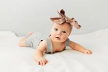 Beautiful Baby Lies On Bed Smiling Bow On Her Head.