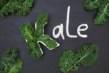 Raw Curly-leaf Kale Cabbage Inside Letter K Shaped Plate, Chalk Inscription KALE And Fresh Green Leafy Vegetables On Blackboard Background. Healthy Food Concept.  Flat Lay Or Top View.