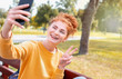Smiling happy red hair student girl taking picture of herself on the phone outside in autumn park