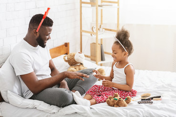 African american girl painting her dad nails, sitting on bed