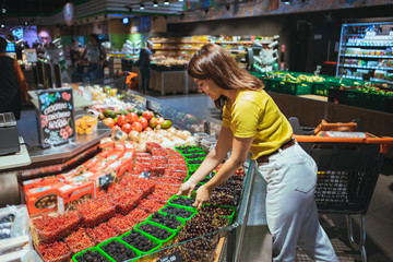 Wall Mural - young woman taking berries from store shelf