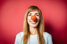 Young Beautiful Woman With A Red Nose Of A Clown On A Pink Background. Concept Red Nose Day, Holiday, Party, Clown