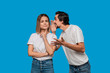 © ianachyrva - Bearded man with mustaches in white t-shirt tells secret to a young blond girl in white t-shirts and blue jeans standing isolated over blue background. Concept of secret telling.