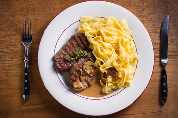 Wall Mural - Grilled beef steaks and noodles in creamy mushroom sauce, garnished with thyme on white plate