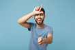 Young laughing man in casual clothes posing isolated on blue wall background, studio portrait. People lifestyle concept. Mock up copy space. Showing loser gesture, pointing index finger on camera.