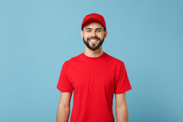 Delivery man in red uniform workwear isolated on blue wall background, studio portrait. Professional male employee in cap t-shirt print working as courier dealer. Service concept. Mock up copy space.