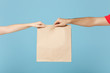 Close up cropped hands hold brown clear empty blank craft paper bag box food for takeaway isolated on blue background. Packaging template mock up. Delivery service concept. Copy space Advertising area