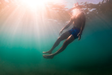Man Rises To Surface Of Water While Diving In Sunlight Dappled U