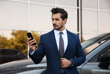 Attractive young man with smartphone near luxury car outdoors