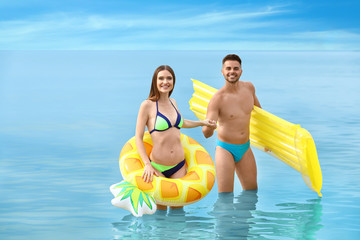 Canvas Print - Young woman in bikini and her boyfriend with inflatable toys on beach. Lovely couple