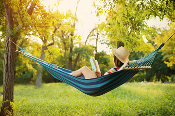 Poster - Young woman reading book in comfortable hammock at green garden