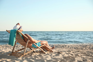 Wall Mural - Young man relaxing in deck chair on beach near sea