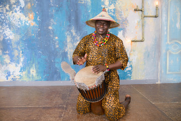 Wall Mural - Handsome african drummer weared in traditional costume playing on djembe drum