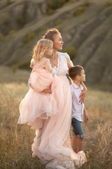 A young mother with children walks in a field at sunset. Country style