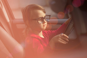 Driving shool. Humorous portrait of cute little child girl learns to drive. Horizontal photo.