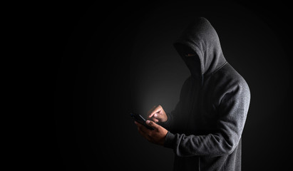 Wall Mural - hacker using smartphone. men in black clothes with hidden face looks at smartphone screen on black b