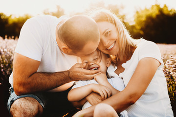 Wall Mural - beautiful young mother and father embracing and kissing their little son outdoor. sweet kid laughing