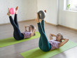 © junky_jess - Pilates abs exercise with small fit ball. Two pretty girls lying on mats and raise up her legs doing workout in fitness studio, selective focus