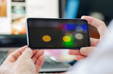 Wall Mural - closeup view man hand holding smartphone with bokeh image on screen.