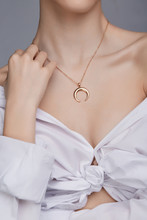 Cropped Shot Of A Lady, Wearing White Chest Tied Shirt. She Has Golden Necklace With Suspension In A Shape Of Half Moon On Her Neck. Her Right Hand Is Touching Shoulder. 