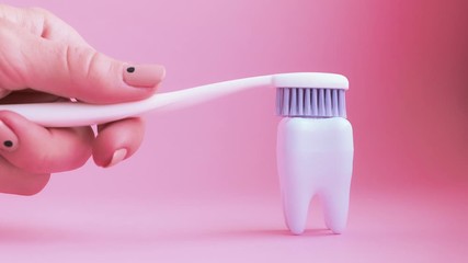 Wall Mural - Female hand brushes big white teeth on pink background. 4K video. Dental care concept.