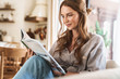 © Drobot Dean - Positive optimistic redhead woman indoors sitting at home reading book or magazine.