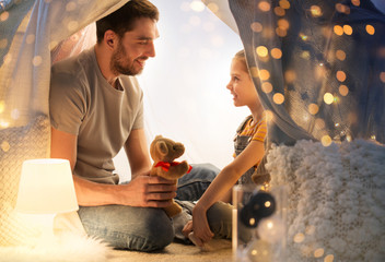 Poster - family, hygge and people concept - happy father with teddy bear toy and little daughter playing in kids tent at night at home