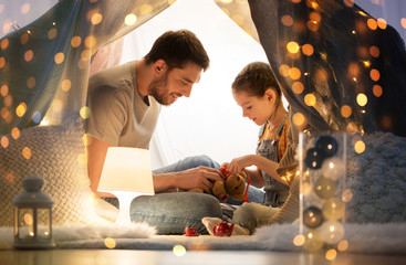 Poster - family, hygge and people concept - happy father with teddy bear toy and little daughter playing in kids tent at night at home