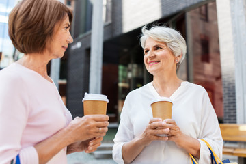 Canvas Print - sale, consumerism and people concept - two senior women or friends with shopping bags drinking takeaway coffee on tallinn city street