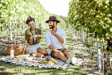 Beautiful Couple Having Romantic Breakfast With Lots Of Tasty Food And Wine, Sitting Together On The Picnic Blanket At The Vineyard On A Sunny Morning