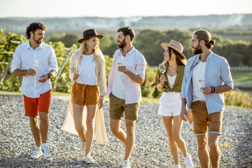 Wall Mural - Group of young friends dressed casually hanging out together, walking with wine glasses on the vineyard on a sunny day