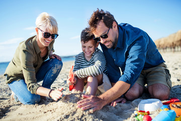 Wall Mural - Young family with small boy sitting outdoors on beach, playing.