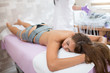© borevina - A young brunette woman is lying on a table in a body care studio waiting for electric muscle stimulation therapy to begin.