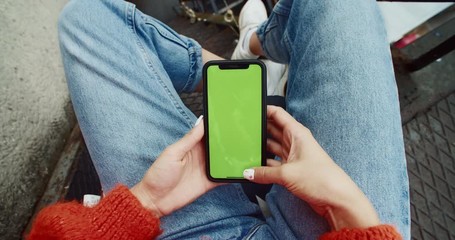 Close-up of busy stylish girl doing tapping and swiping gestures on mobile green blank screen with mockup technology. first-person view woman browsing on smartphone.