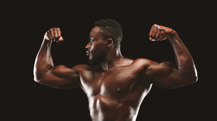 Wall Mural - Athletic black guy flexing muscles over black studio background