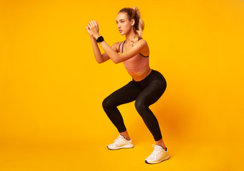 Wall Mural - Young Woman Doing Deep Squat Exercise Over Yellow Background