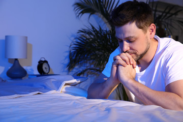 Sticker - Handsome man saying bedtime prayer in dark room at night. Space for text