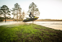 Man Teen Boy Riding A Personal Watercraft And Jumping Over A Peninsula At Sunset On A Small Lake Pond