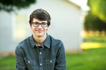 teenage boy with glasses outside on a spring day sitting outside of a house home smiling