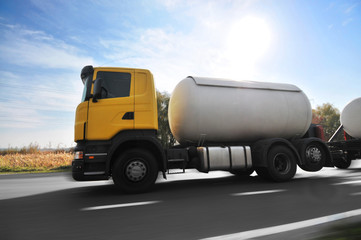 Wall Mural - Big metal fuel tanker truck shipping fuel on the countryside road in motion against sky with bright sun